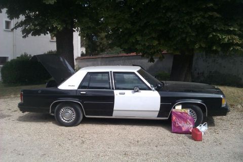 1991 Ford LTD Crown Victoria - Side view of a black and white 1991 Ford Crown Victoria with its trunk open, parked on gravel.