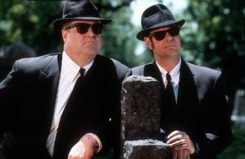 1991 Ford LTD Crown Victoria - Two men dressed in black suits and hats, possibly from a movie scene, are shown outdoors.