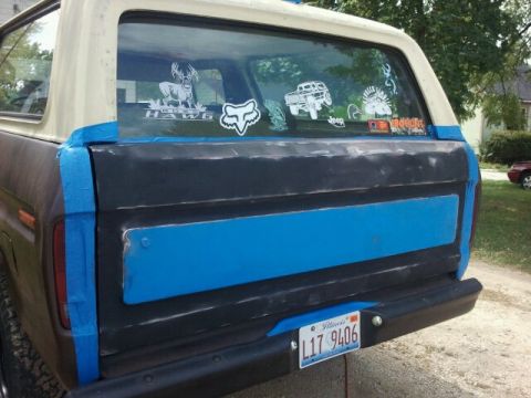 1979 Ford Bronco - The rear of a 1978 Ford Bronco shows a blue stripe and tape around the tailgate, with various stickers on the rear window.