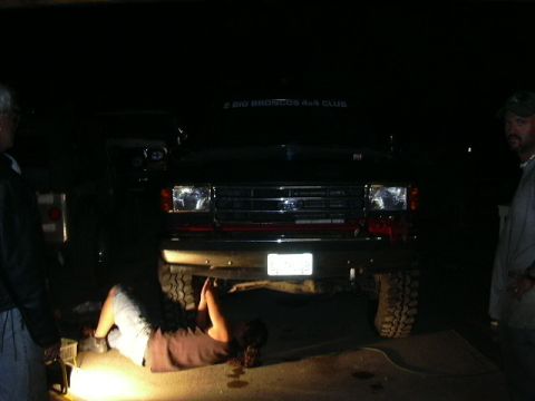 1991 Ford Bronco - A person works on the underside of a black Ford Bronco, with another vehicle partially visible to the left.