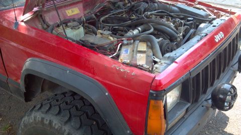 1995 Jeep Cherokee - The engine bay of a red 1995 Jeep Cherokee is visible with the hood raised.