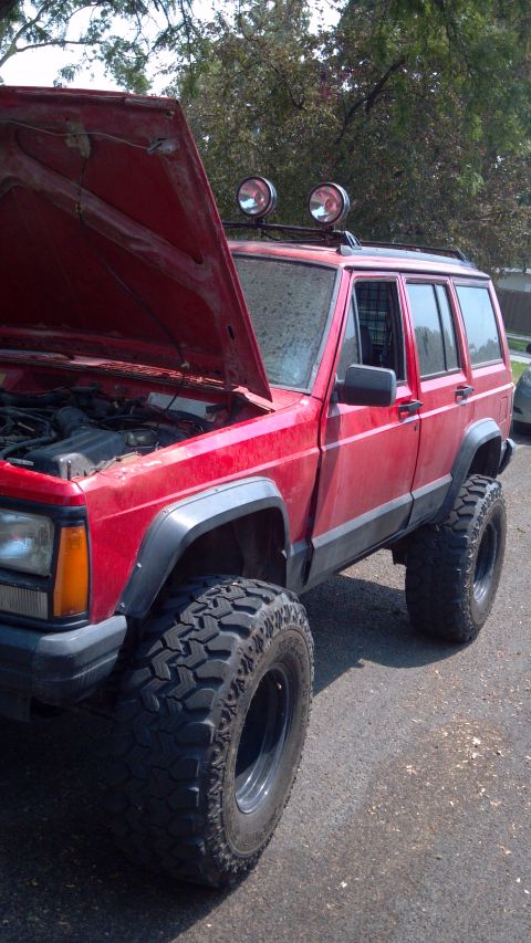 1995 Jeep Cherokee - This red Jeep Cherokee has been modified with a lifted suspension and large off-road tires, and its hood is open.