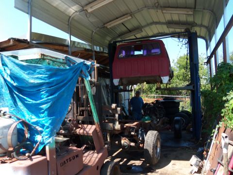 1987 Ford Ranger - Workshop scene with a red pickup truck cab elevated on a lift, alongside a forklift and various vehicle components.