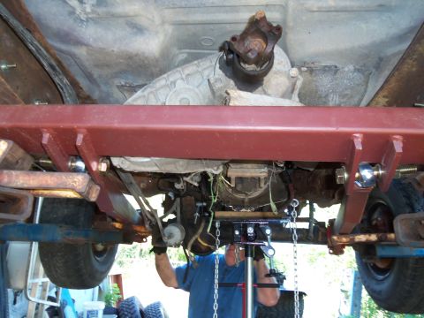1987 Ford Ranger - Mechanic works on the transmission and driveshaft assembly underneath a truck.