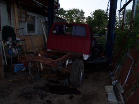 1987 Ford Ranger - The body of a red pickup truck is elevated above its chassis, which is supported by jack stands.