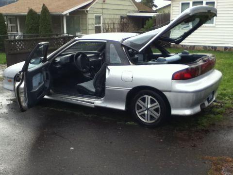 1990 Geo Storm GSi - Silver hatchback with driver's door and rear hatch open, showing the interior and cargo area.