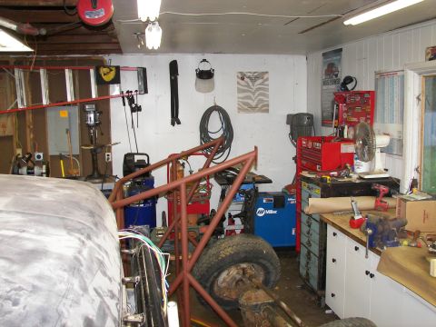 1988 Ford Bronco - A cluttered garage scene shows a vehicle frame under construction alongside various tools and equipment.