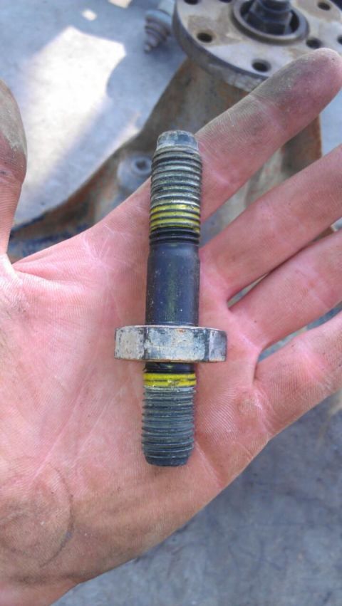 1998 Ford Crown Victoria - person holds a double-ended threaded stud with a hex shoulder in their palm above a greasy flanged part.