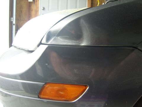 2007 Ford Mustang - Close-up of a dented car fender with an amber turn signal light.