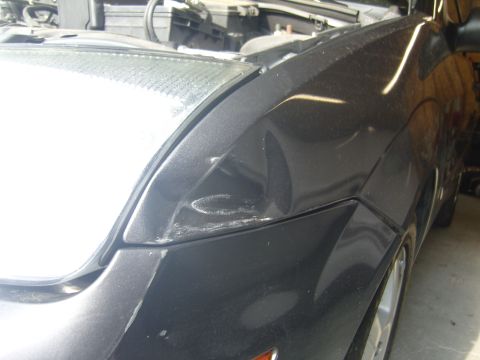 2007 Ford Mustang - A damaged dark gray car fender is visible with the hood open, revealing engine parts.