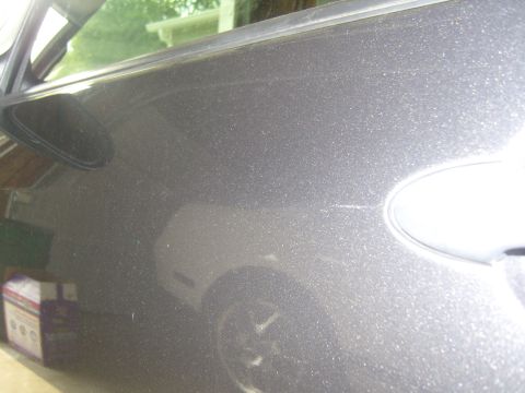 2007 Ford Mustang - Scratches are visible on the metallic paint of a car door, with a reflection of the vehicle's wheel in the lower portion.