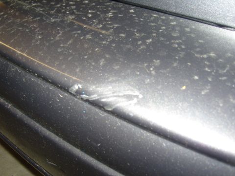 2007 Ford Mustang - Close-up of a damaged dark gray bumper, showing a dent and scuffing.