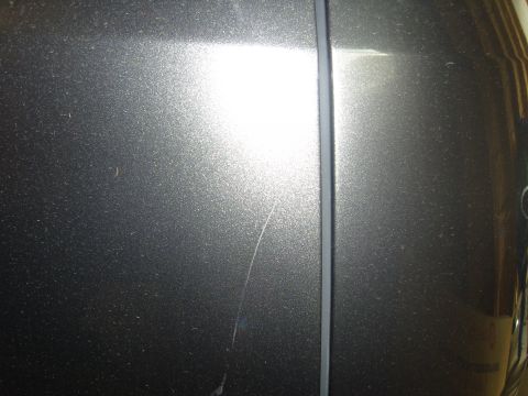 2007 Ford Mustang - Closeup of a metallic silver-gray painted body panel beside black rubber trim, showing a fine scratch and glare.
