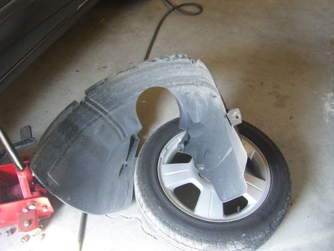 2007 Ford Mustang - A car fender liner and tire are shown on a concrete floor, with a red car jack nearby.