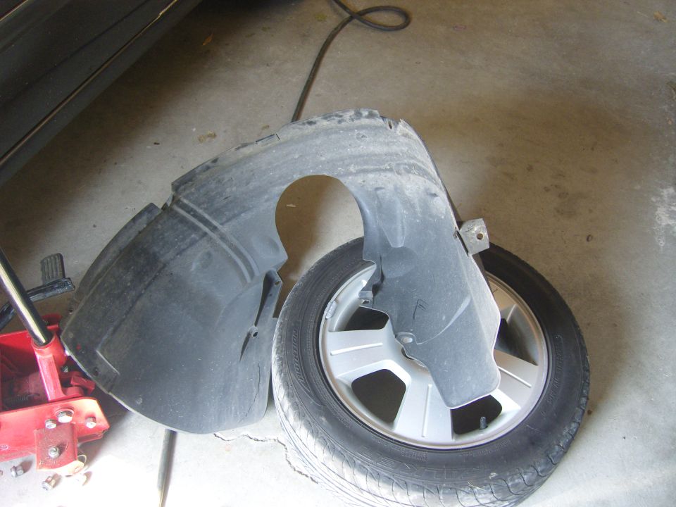 Car fender liner and tire on concrete floor next to a red car jack