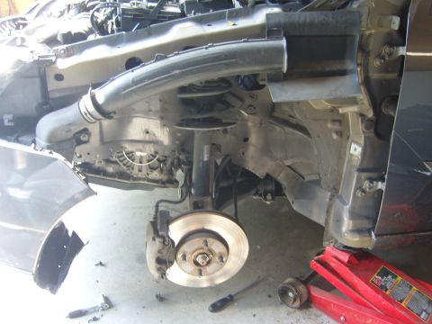 2007 Ford Mustang - The front wheel assembly of a car is shown with the fender detached and brake components removed, indicating repair work.