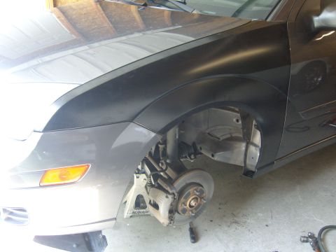 2007 Ford Mustang - The front fender and wheel well of a gray car are visible, supported by jack stands, indicating repair work is in progress.