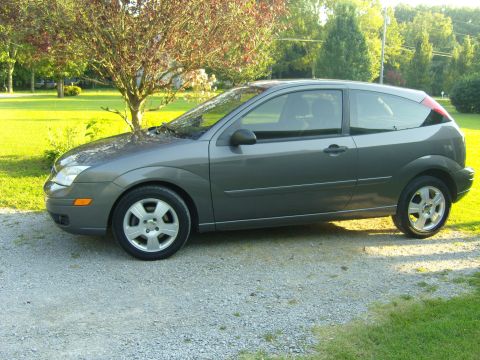 2007 Ford Mustang - A gray 2007 Ford Focus hatchback is parked on a gravel driveway with a tree and green lawn in the background.
