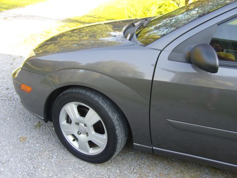 2007 Ford Mustang - The front passenger side of a gray sedan is shown parked on a gravel surface.