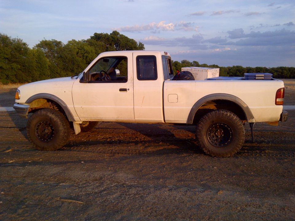 White Ford Ranger pickup truck, side view, lifted suspension, off-road tires, aftermarket wheels, cargo in bed, dirt road