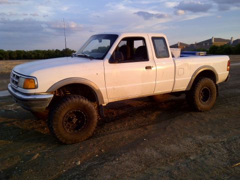 1994 Ford Ranger - A white pickup truck with aftermarket wheels and tires sits on a dirt lot under a cloudy sky.