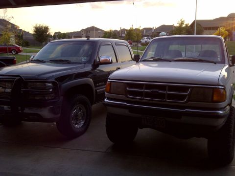 1994 Ford Ranger - Two pickup trucks, a silver 1994 Ford Ranger and a black truck, are parked in front of houses.