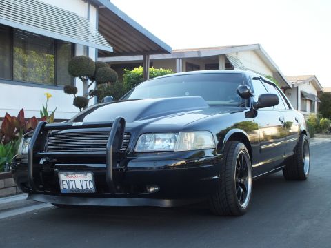 2003 Ford Crown Victoria - Lowered black sedan shows its grille guard, hood scoop and tinted windows in a home driveway.