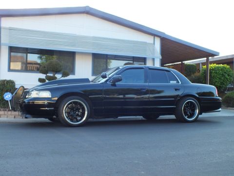 2003 Ford Crown Victoria - Low-slung black sedan shown in profile with deeply tinted glass and polished-lip wheels.