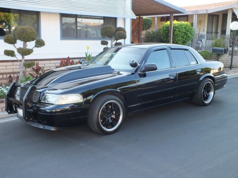 2003 Ford Crown Victoria - Blacked-out sedan parked on a street showing its push bumper, scooped hood and dark wheels.