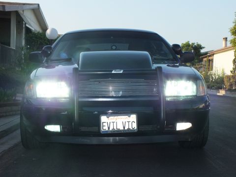 2003 Ford Crown Victoria - Front view of the blacked-out sedan glowing with HID headlights and fog lamps at dusk.