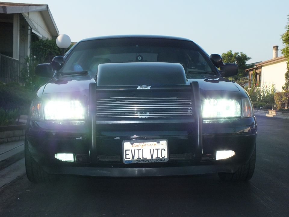 Black Ford Crown Victoria with headlights on at twilight and brush guard
