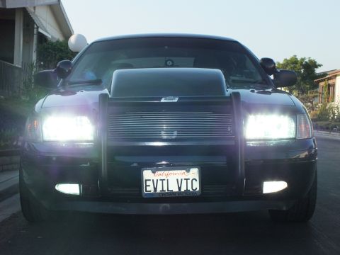 2003 Ford Crown Victoria - Dusk head-on view of the sedan with lights on, push bumper and billet grille visible.