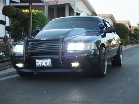 2003 Ford Crown Victoria - Angled front view of the lowered sedan with lights lit, hood scoop and push bumper.