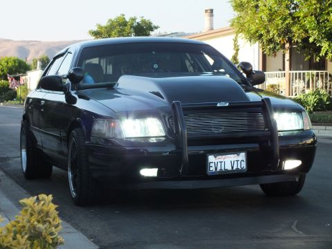 2003 Ford Crown Victoria - Front three-quarter action shot of the sedan in motion with lights illuminated.