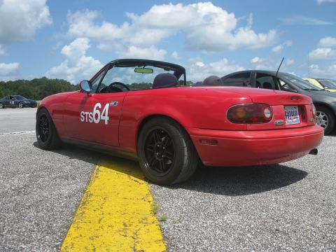 1991 Mazda Miata - A red convertible sports car is parked on a track, with a yellow line marking the edge of the pavement.