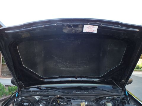 2003 Ford Crown Victoria - View under the raised hood showing the liner, scoop opening and a hood-pin install warning label.