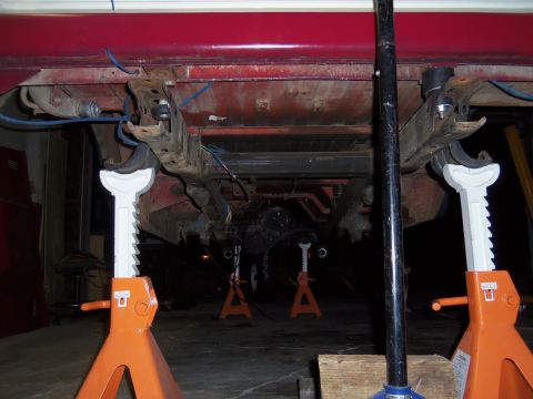 1968 Ford Bronco - The underside of a red vehicle is elevated on jack stands, revealing its suspension and drivetrain components.