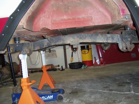 1968 Ford Bronco - Underbody of a vehicle supported by jack stands in a garage, with various tools and parts around.
