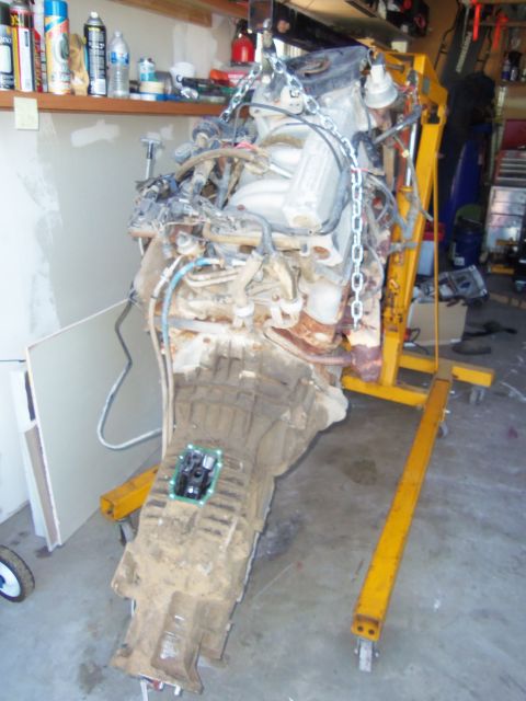 1968 Ford Bronco - An engine and transmission assembly is suspended by a yellow engine crane in a garage setting.