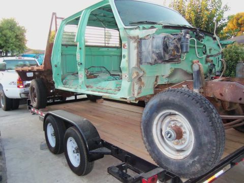 1968 Ford Bronco - A green truck cab, stripped down and on a trailer, is towed by another truck.