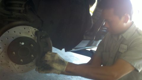 2003 Ford Crown Victoria - Technician grips a brake caliper at a slotted front rotor on a raised vehicle in a shop.