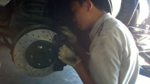 2003 Ford Crown Victoria - Gloved worker leans in to seat a caliper over a five-lug slotted rotor on a lifted car.
