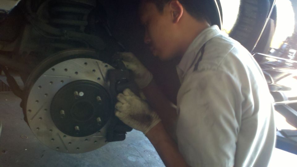 Mechanic leaning into wheel well fitting caliper over drilled brake rotor