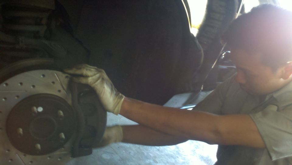 Mechanic in gloves reaching behind drilled front brake rotor on raised car
