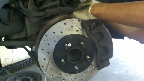 2003 Ford Crown Victoria - Slotted and drilled rotor seated on a five-stud hub with a black caliper, gloved hand above.