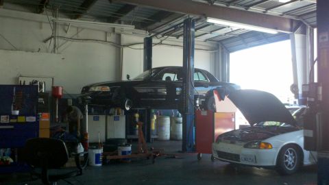 2003 Ford Crown Victoria - Sideways shop scene shows cars raised on hoists with bays, hoses, and equipment around.