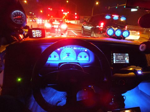 2003 Ford Crown Victoria - Glowing blue dash and aftermarket gauges face a lit road with brake lights and an SUV ahead.