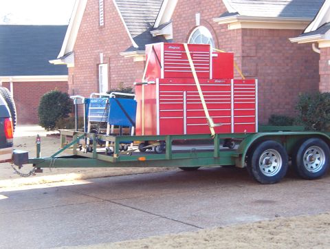 2004 Land Rover Land Rover - A trailer carries stacked red toolboxes and blue carts in front of a brick house.
