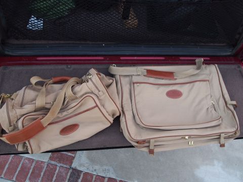 1994 Ford Bronco - Two pieces of tan canvas luggage with brown leather trim and oval logo patches, a duffel bag and a garment bag, sitting on the carpeted rea…