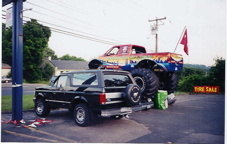 Black Ford Bronco parked next to a monster truck with a city skyline painted on its side